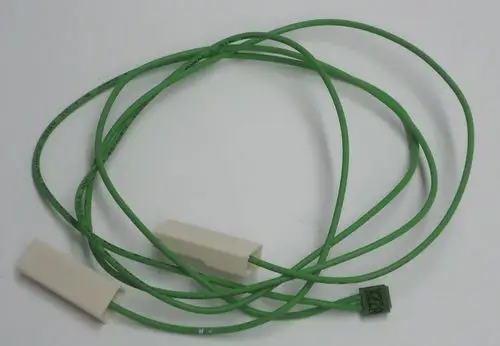 Grünes Kabel mit zwei weißen Anschlüssen, möglicherweise für Daikin Produkte, liegt auf einem hellen Hintergrund.
